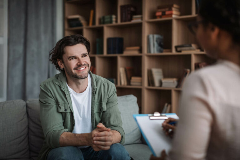 A man sits on a couch while speaking to a counselor.