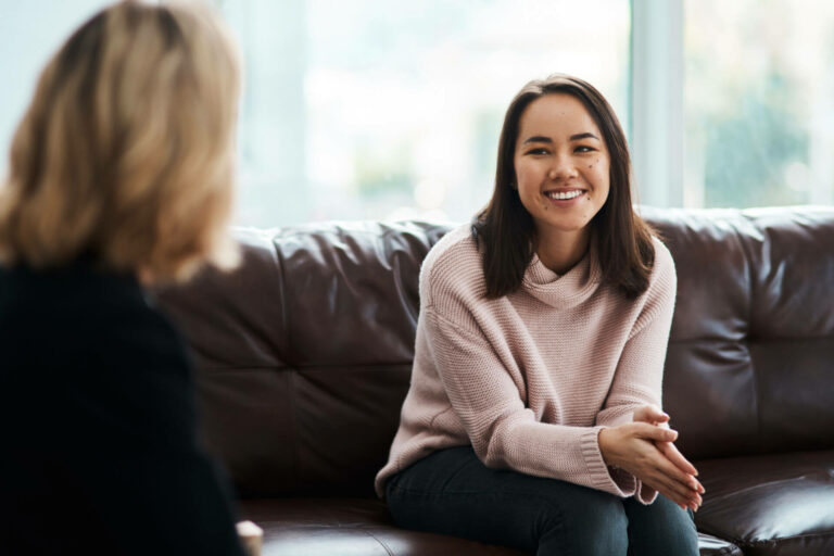 A woman sits on a couch while speaking to a counselor.